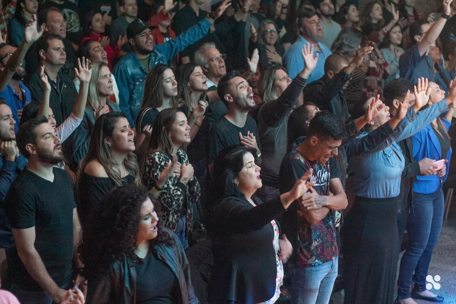 A packed room worshipping with hands raised