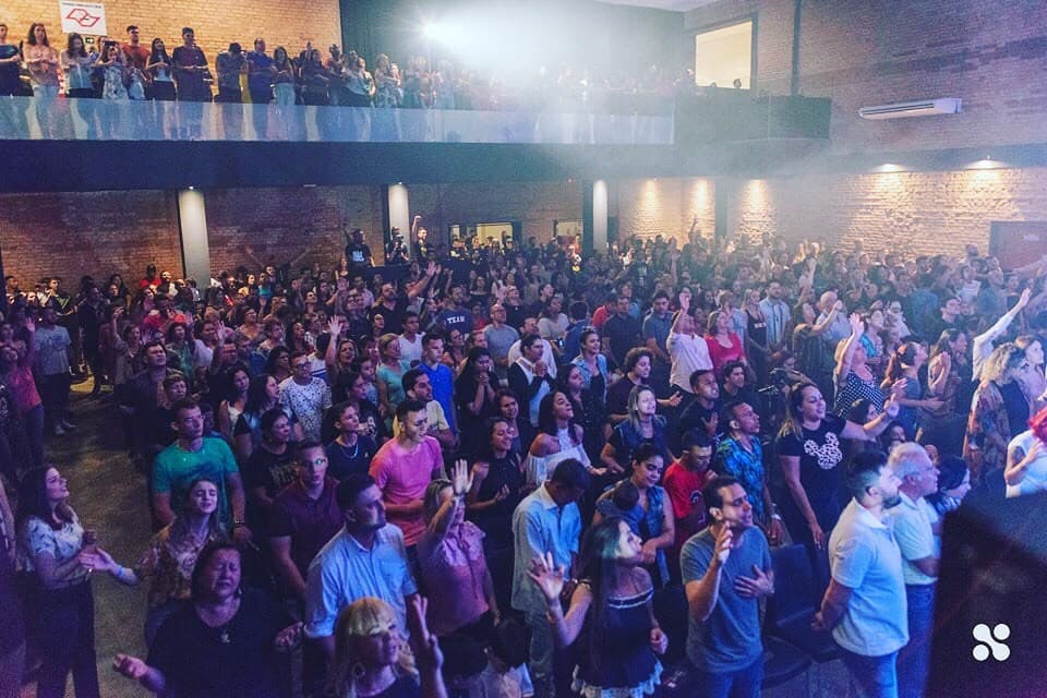 A packed church seen from the balcony, people standing in worship