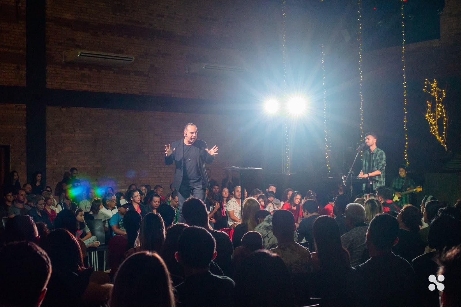 Pastor Claudinei preaching on stage under the lights, the room full
